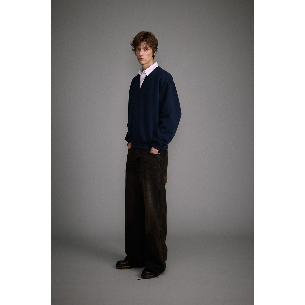Model wearing an oversized navy V-neck sweatshirt over a pale pink striped shirt with dark wide-leg trousers.