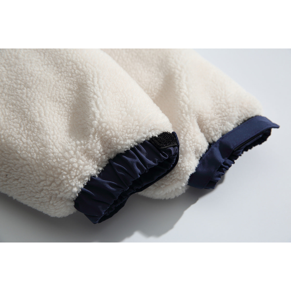 Close-up of ivory fleece sleeves with navy cuffs and hook-and-loop adjusters.