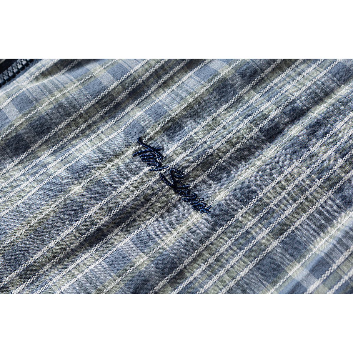 Close-up of dark embroidered script on blue-gray plaid shirt fabric.
