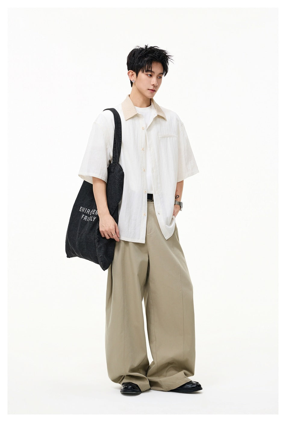 Full-length model wearing an ivory short-sleeve shirt with a beige collar, khaki wide-leg trousers, and carrying a dark tote.