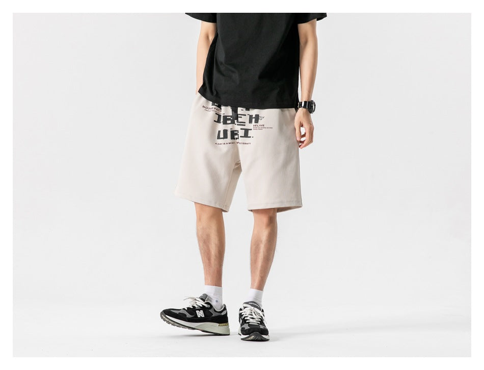 Model wearing khaki graphic-print shorts with a black tee and sneakers, three-quarter view, cropped at chest