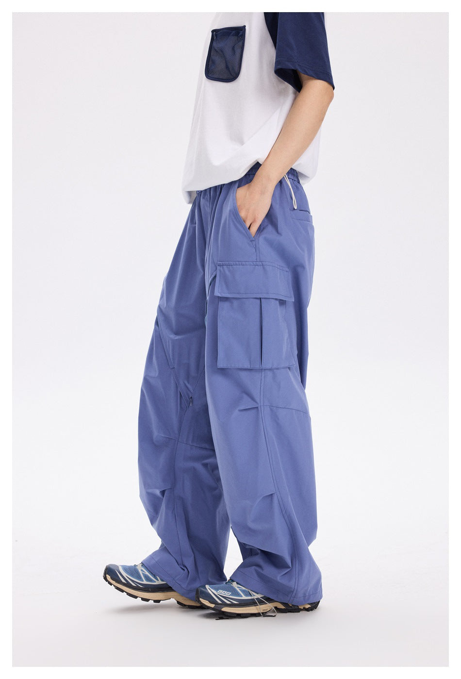 Side view of a model wearing loose periwinkle cargo pants with a large flap pocket and white drawcord.