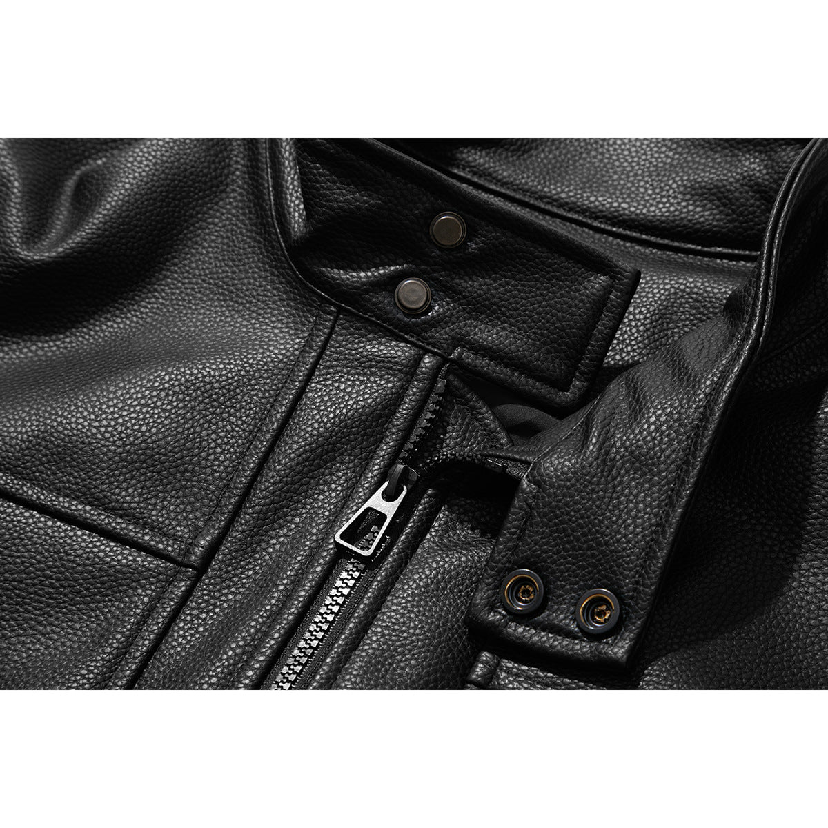 Close-up of a black pebbled jacket's zipper, snap fasteners and overlapping front tabs.