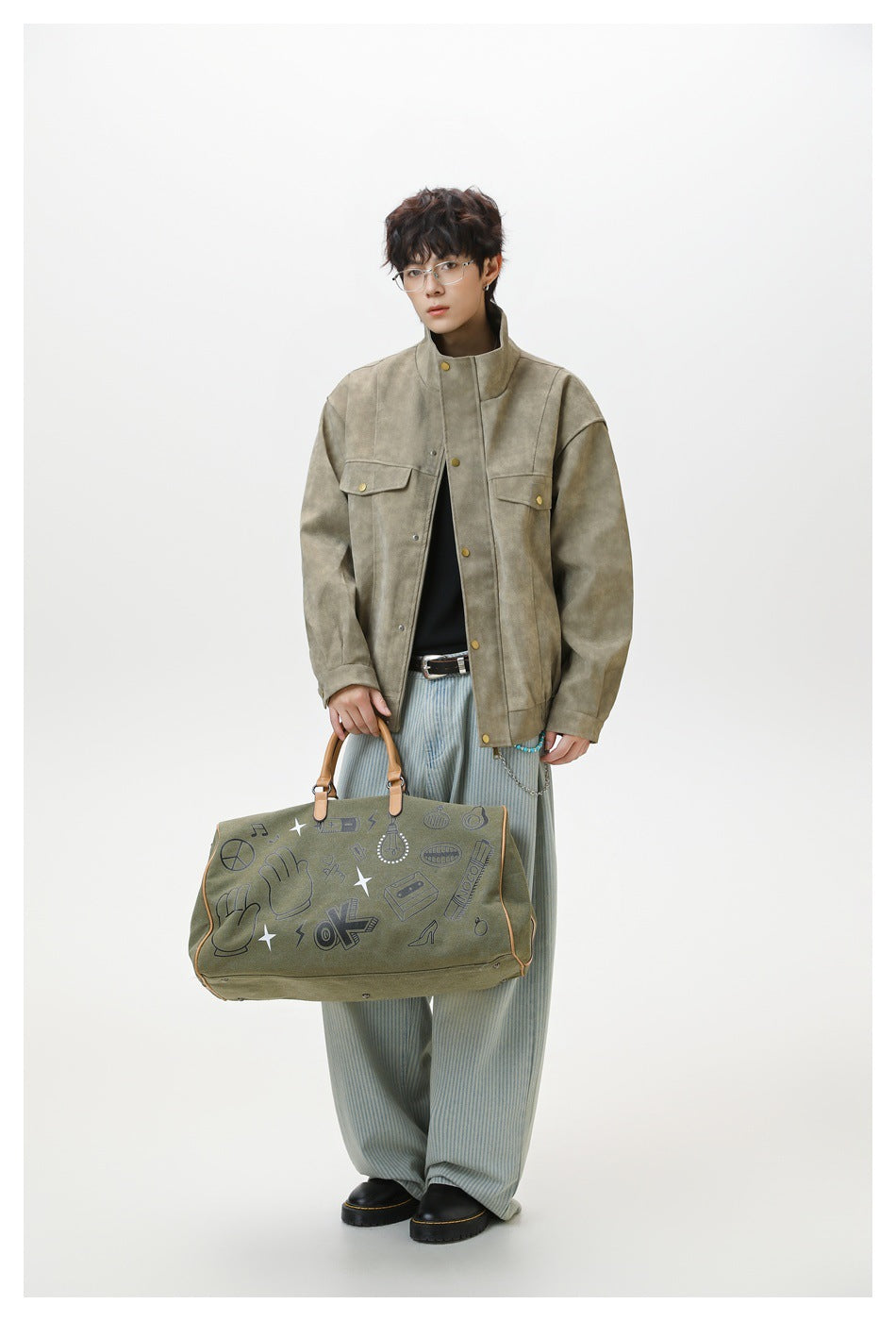 Full-length model wearing an olive-gray jacket and carrying a large printed olive bag.