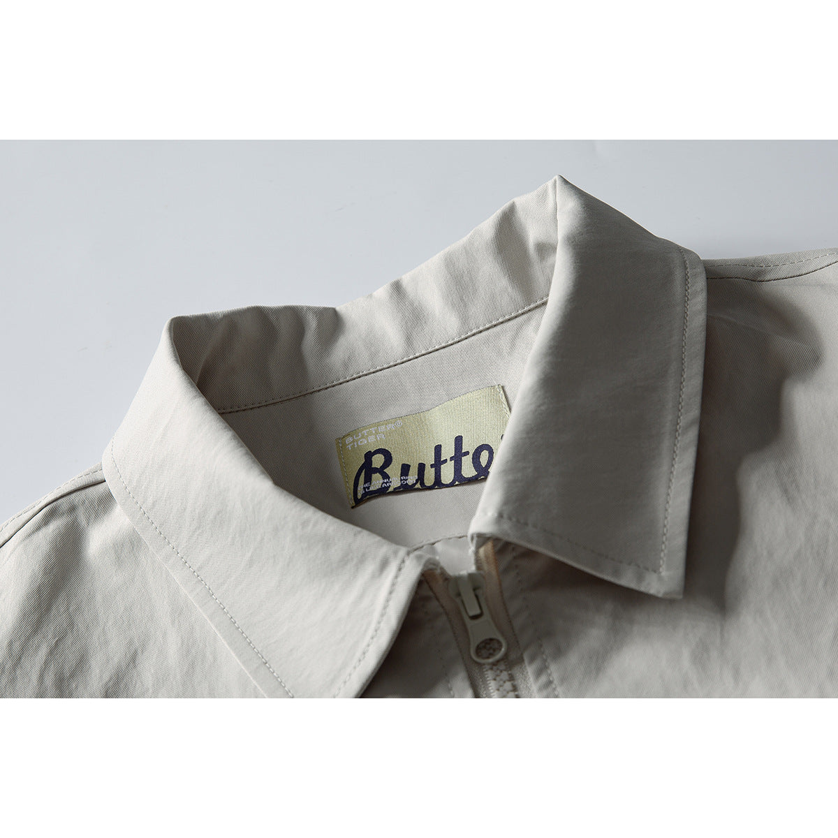 Close-up of a light gray jacket's pointed collar, zipper, and sewn-in neck label.