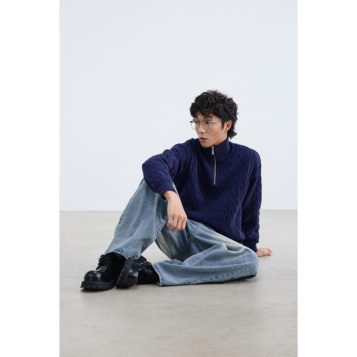 Seated model wearing a navy cable-knit quarter-zip sweater, light blue jeans, and black boots.
