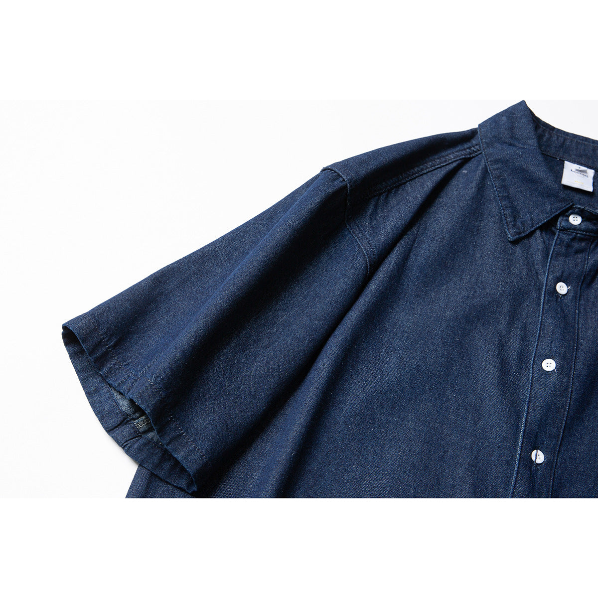 Close-up of a dark indigo shirt sleeve, shoulder seam, collar and front placket with white buttons.