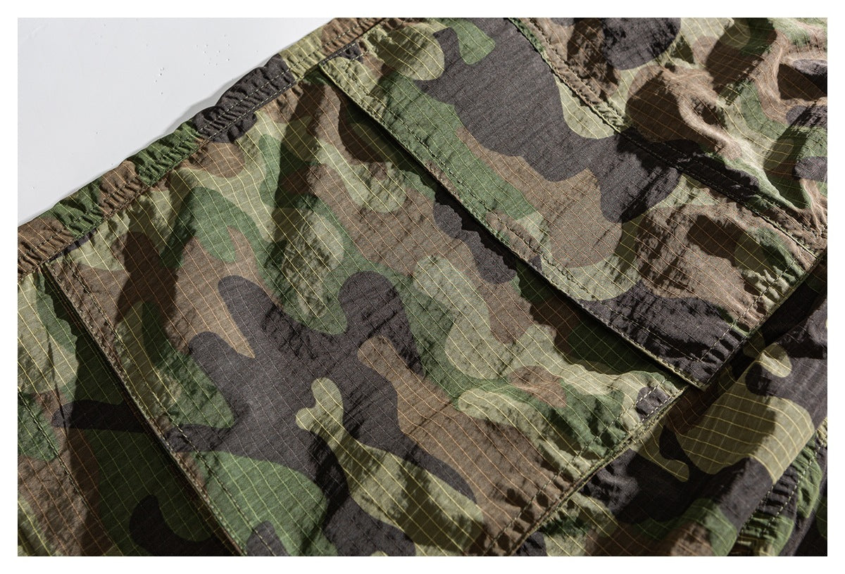 Close-up of a green, brown, and black camouflage garment with fine grid lines and a stitched pocket.