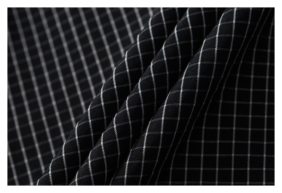 Close-up of folded black fabric with a thin white grid pattern and visible texture.