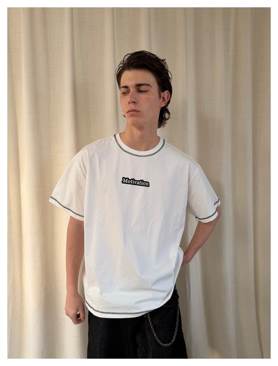 Model wearing a white T-shirt with black contrast stitching and a small black chest graphic.