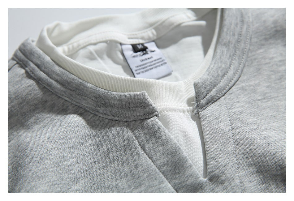 Close-up of a heather-gray sweatshirt's white crew neck and front placket, with the inner neck label visible.