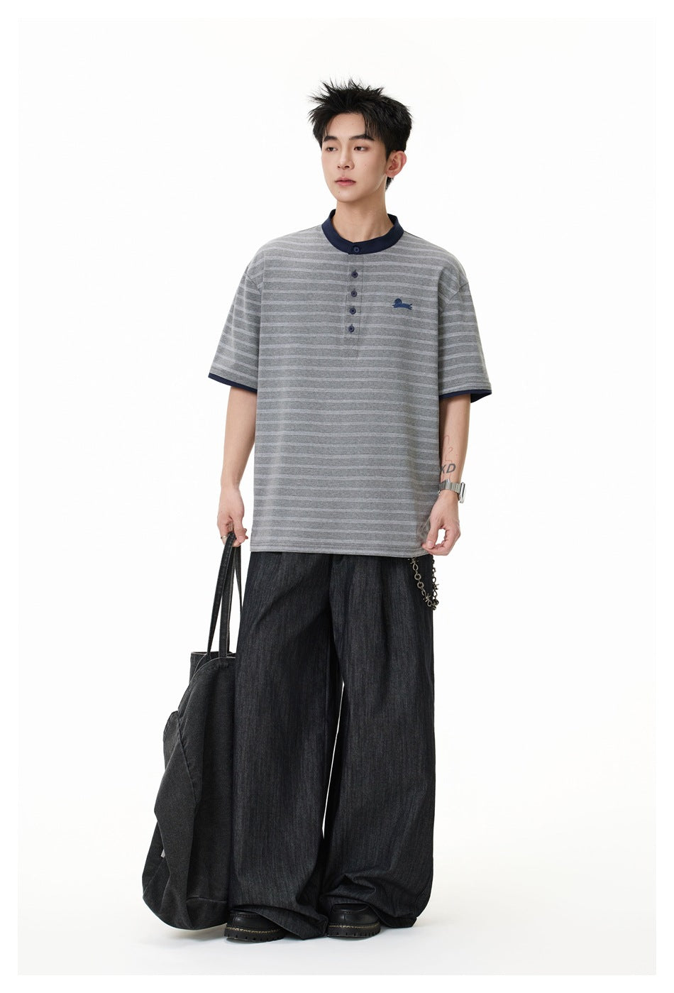 Full-length model wearing a gray striped henley with navy trim and loose dark trousers, carrying a black tote.