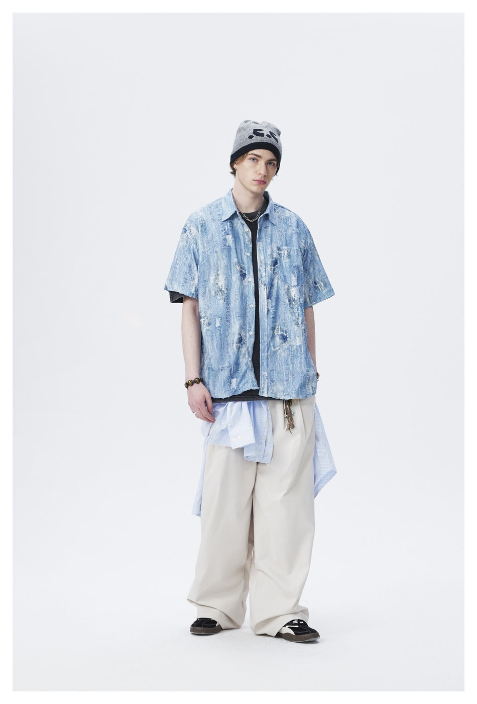 Model wearing a light blue distressed short-sleeve shirt open over a dark tee with wide beige pants and a gray beanie
