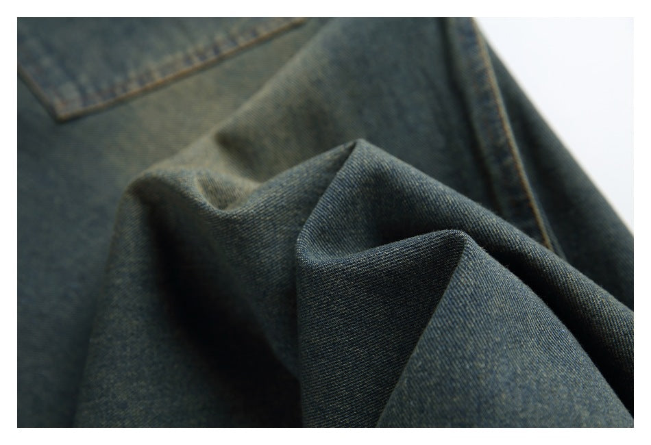 Close-up of dark indigo denim trouser fabric folded to show its texture and a stitched pocket edge.