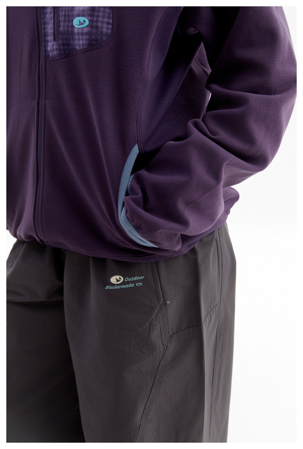 Close-up of a person wearing a plum jacket with a patterned chest pocket and a dark logo-printed pants leg.