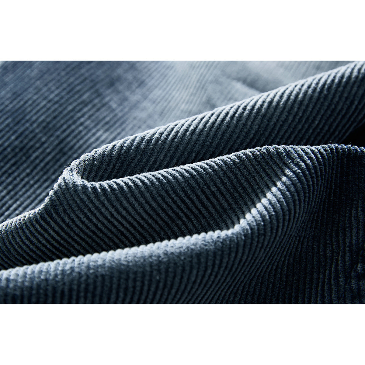 Macro view of dark blue corduroy fabric folded to show its raised ribs and stitched edge.