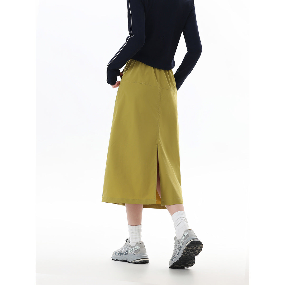 Back view of a model wearing a mustard-olive midi skirt with a center seam and back slit.