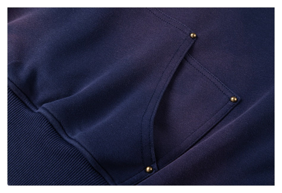 Close-up of navy garment with a stitched pocket flap, three small brass-tone snaps, and ribbed trim.