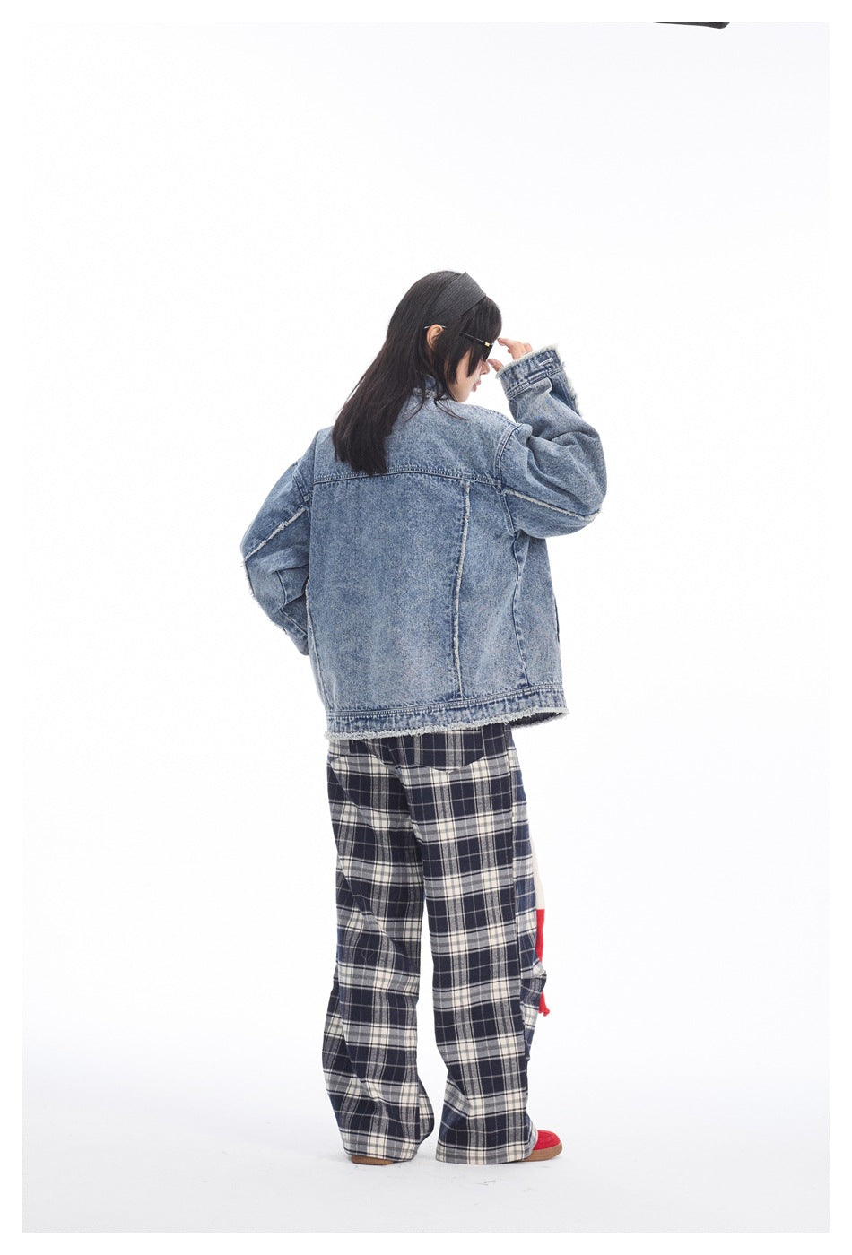 Rear view of a model wearing an oversized blue acid-wash denim jacket with frayed edges and dark plaid trousers.