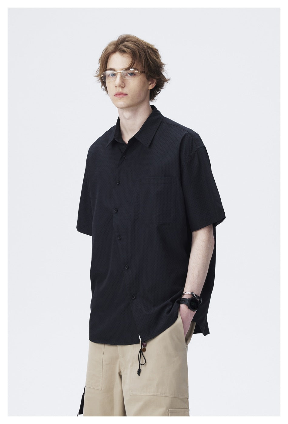 Model wearing a black short-sleeve button-up shirt with a subtle texture and chest pocket, shown from the front at an angle.