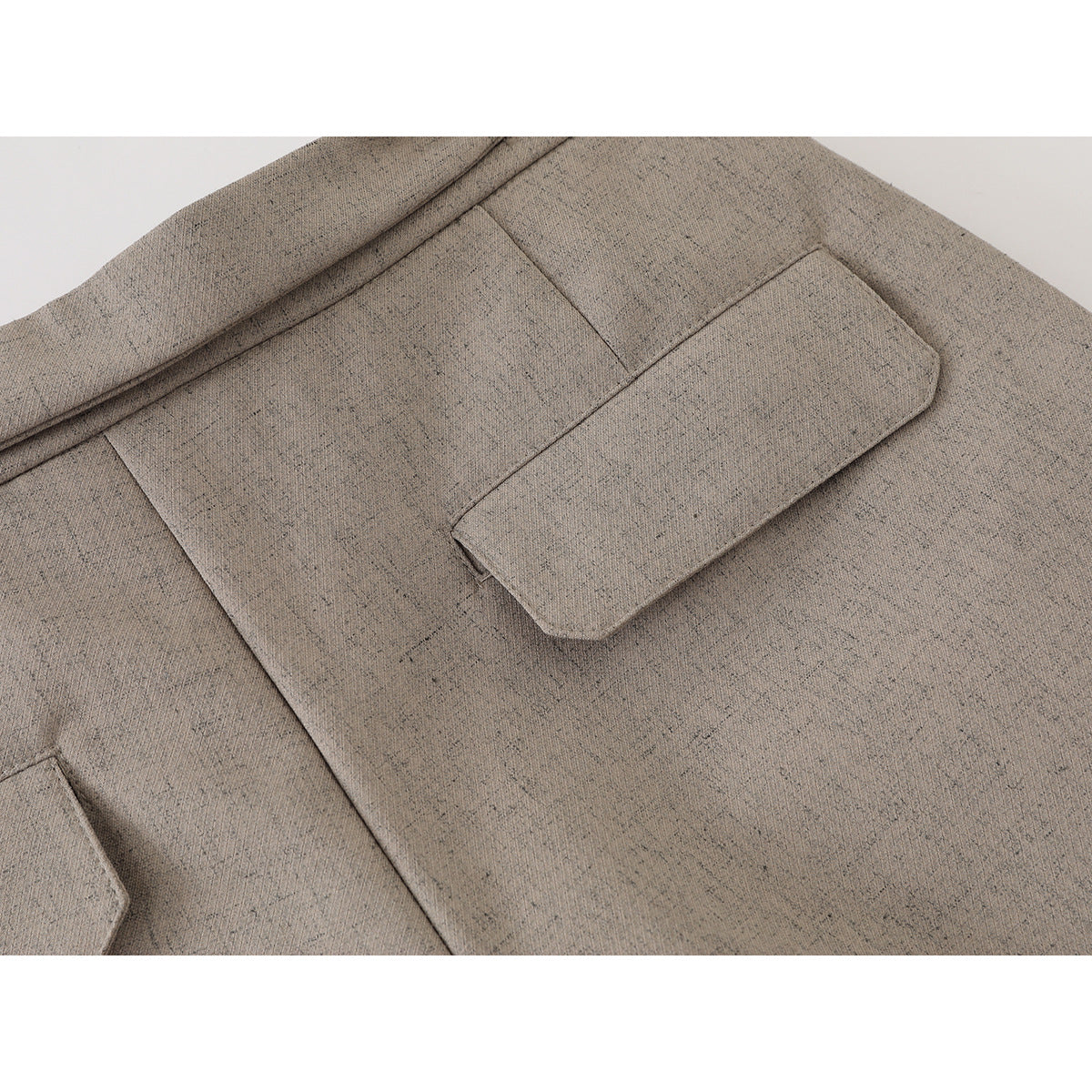 Close-up of taupe trousers showing a flap pocket and the fine speckled fabric surface.