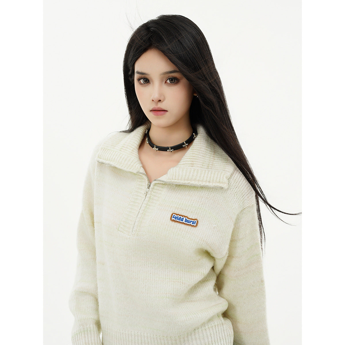 Model wearing an ivory knit pullover with a wide collar, short zipper, and small chest patch.