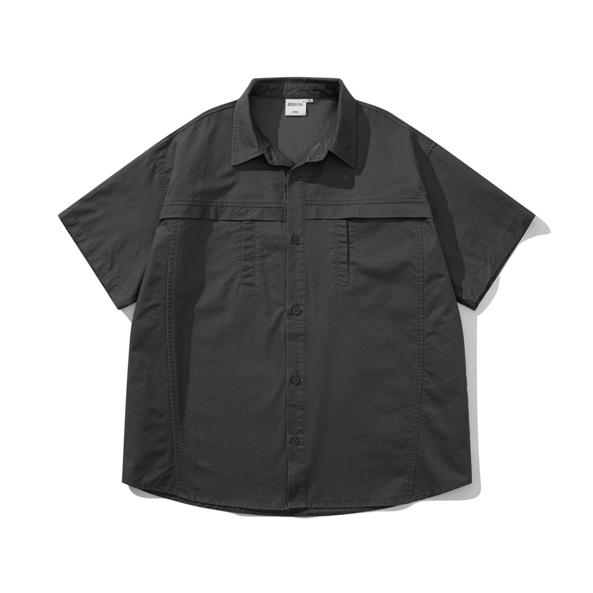 Black-gray short-sleeve button-front shirt flat lay with chest yoke seam, two chest pocket openings and curved hem