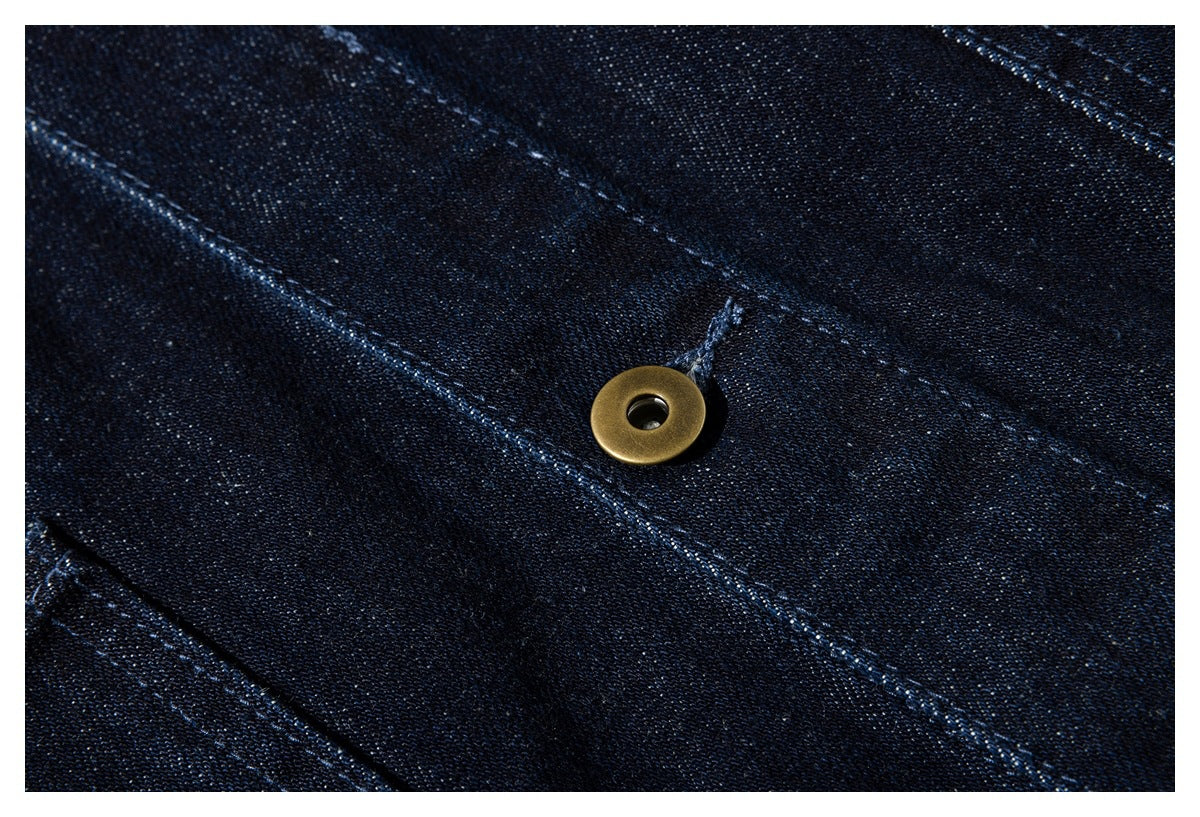 Close-up of a brass-colored snap fastener on dark indigo denim with diagonal stitching.