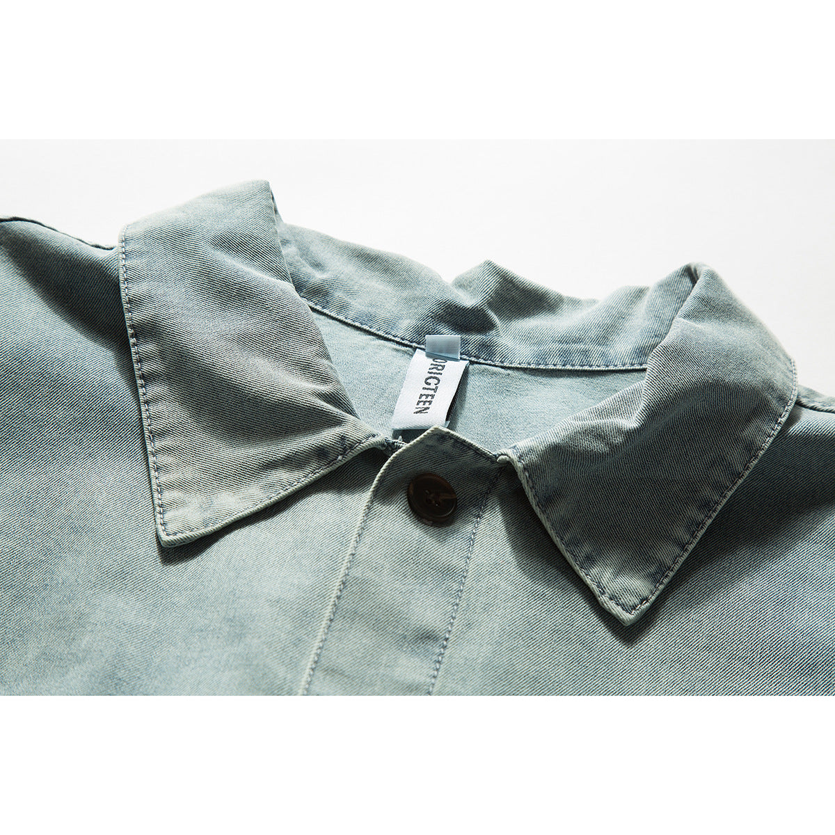 Close-up of a light blue denim shirt collar, dark button and sewn-in white neck label.