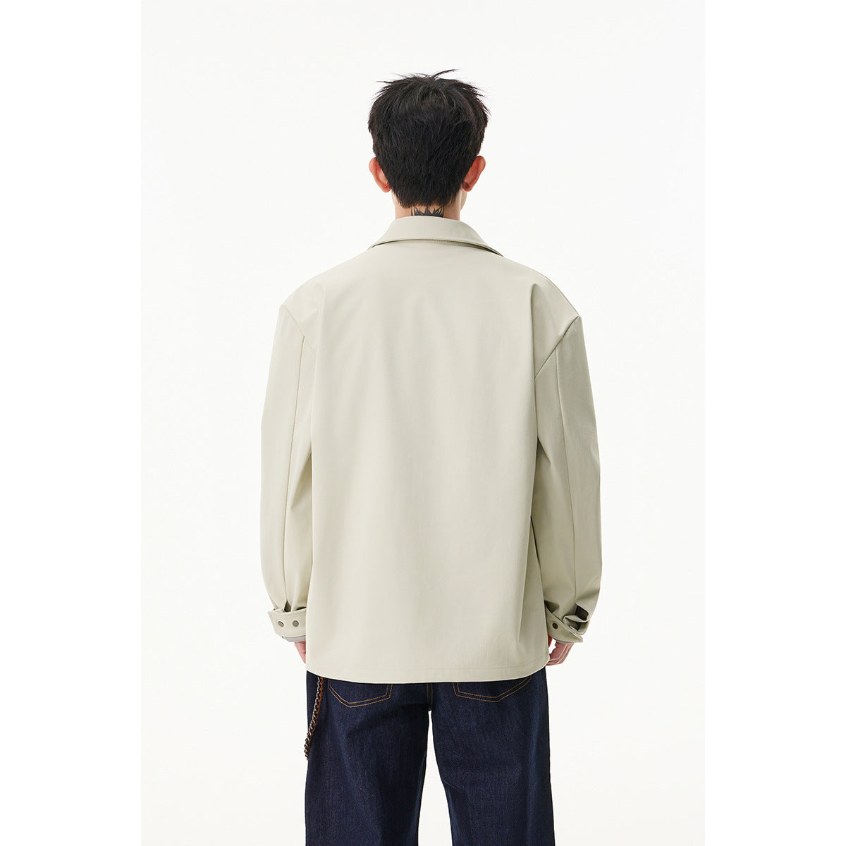 Back view of a model wearing a light cream jacket with a collar and cuff tabs, paired with dark jeans.