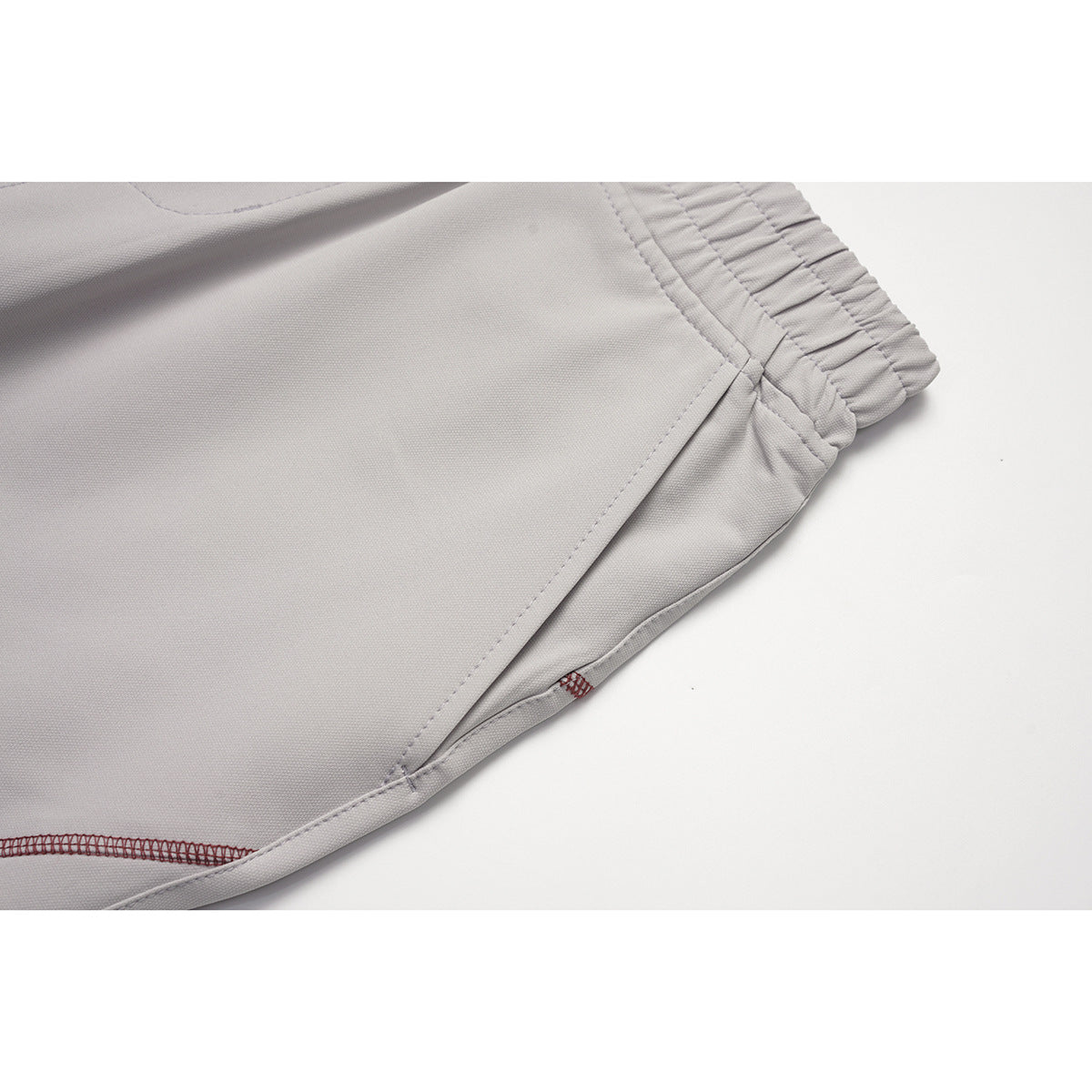 Close-up of light gray pants showing the elastic waistband edge and diagonal panel stitching.