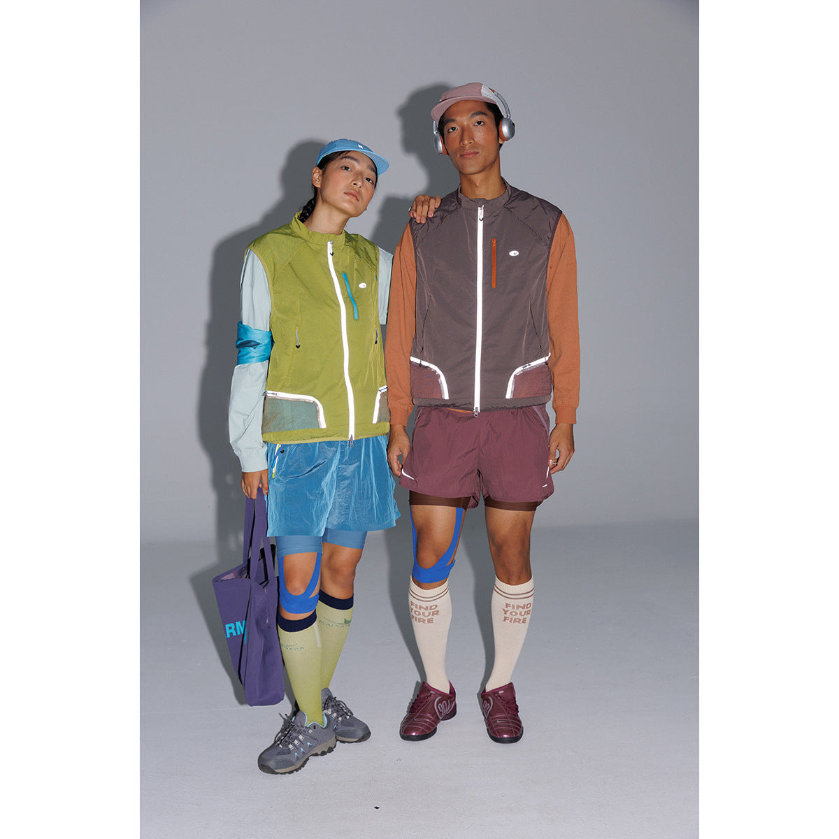 Two models wearing color-blocked zip-front running vests with athletic shorts, knee-high socks, caps and sneakers.