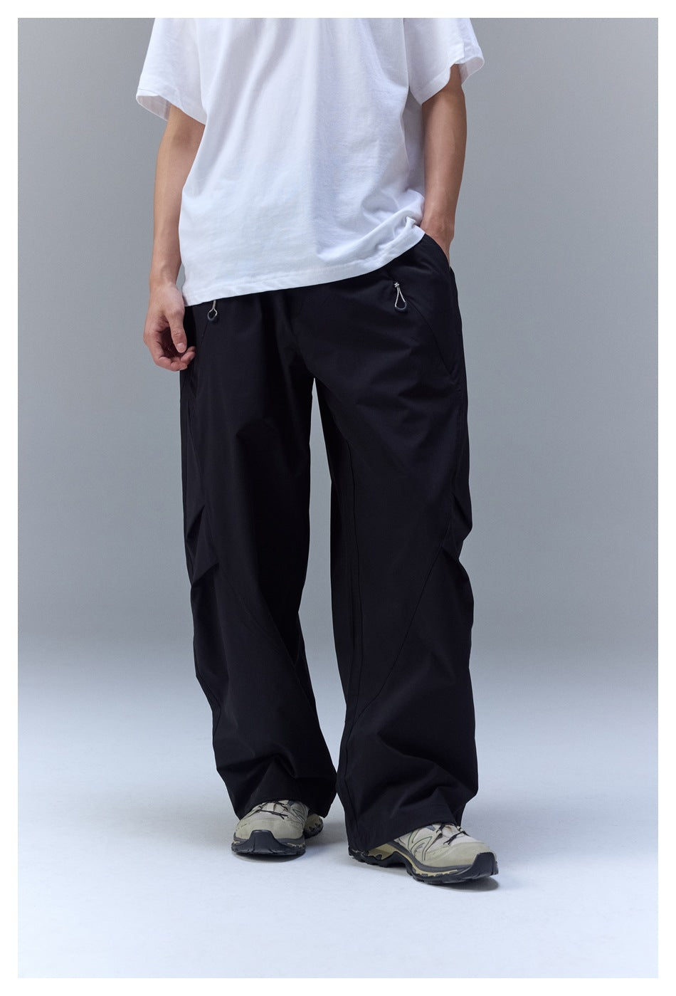 Model wearing loose black wide-leg pants with zip pockets, paired with a white T-shirt and sneakers, front view.