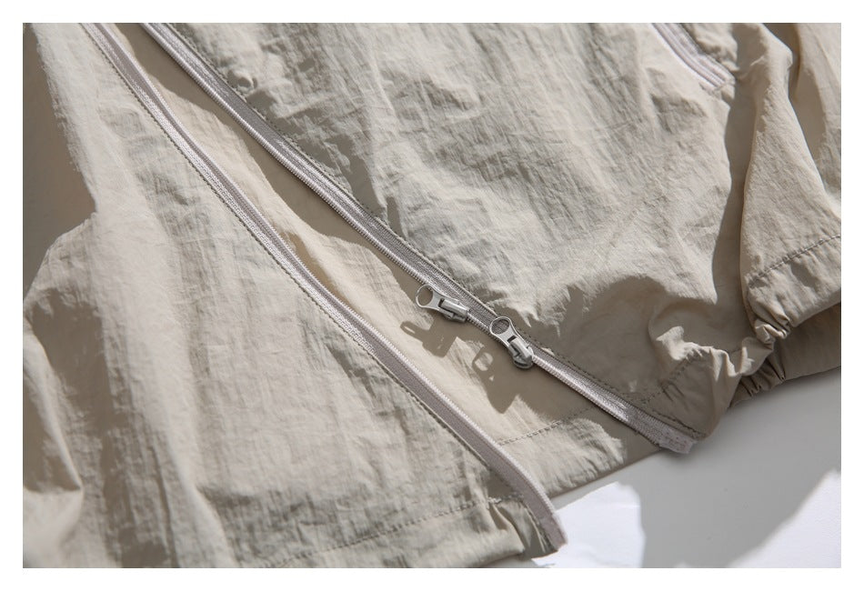 Close-up of a light beige garment showing a pale zipper and double-slider metal pulls.