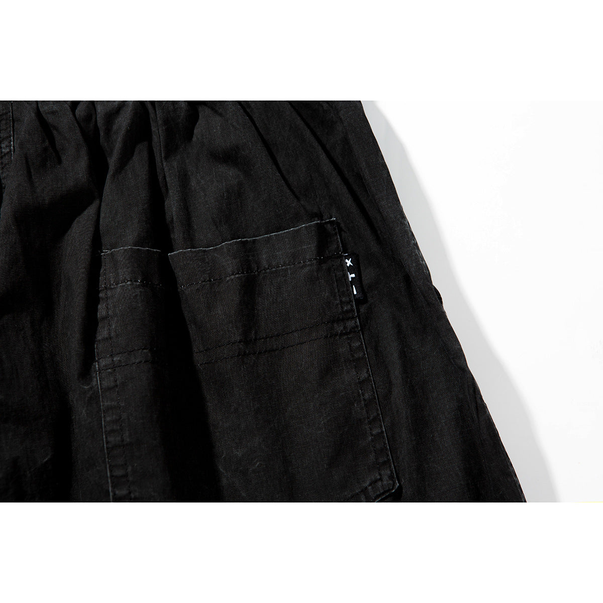Close-up of a rectangular pocket and stitching on black shorts, with a small sewn side tag.