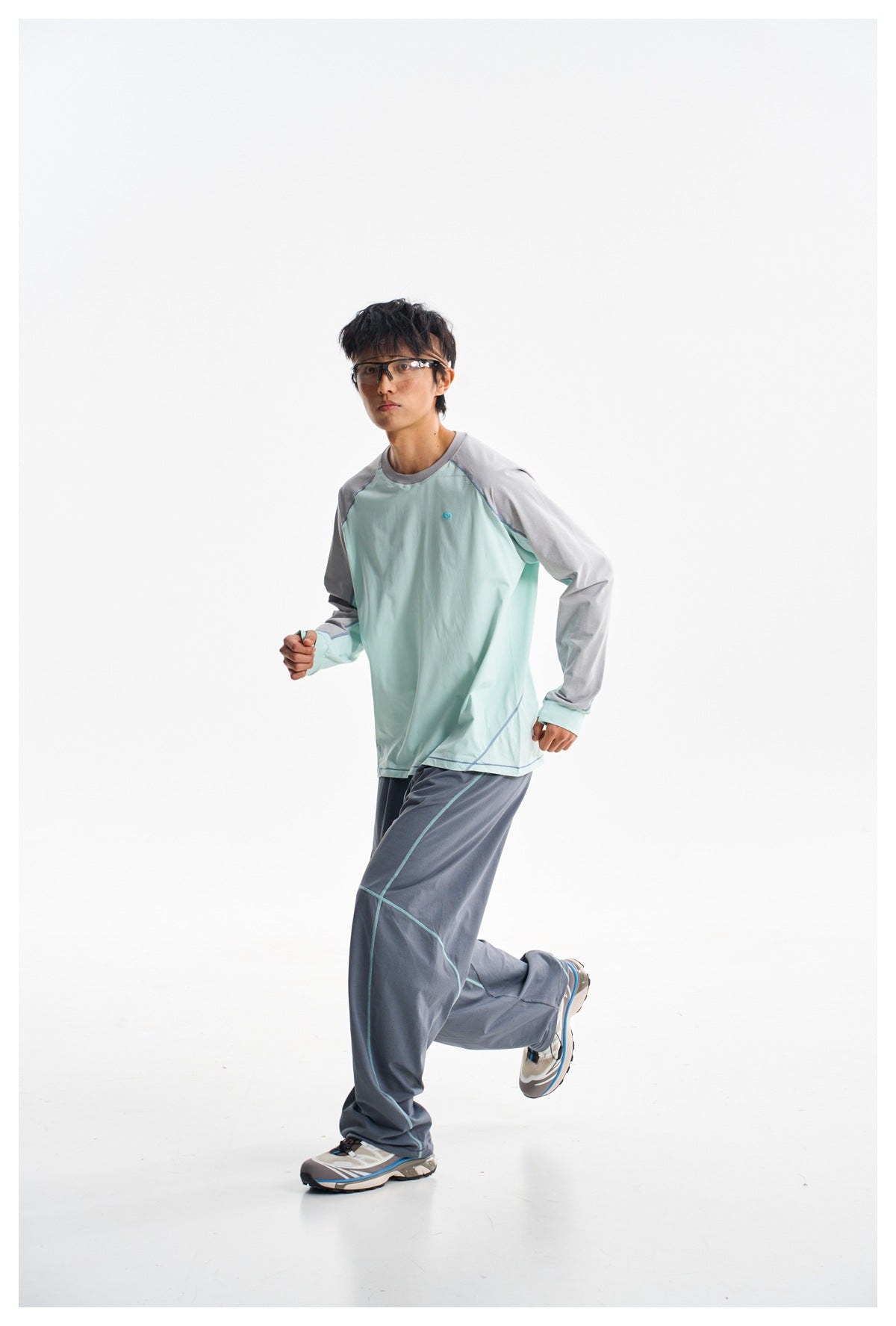 Model in a mint-green and gray long-sleeve shirt and slate-blue trousers, shown in a mid-stride pose.