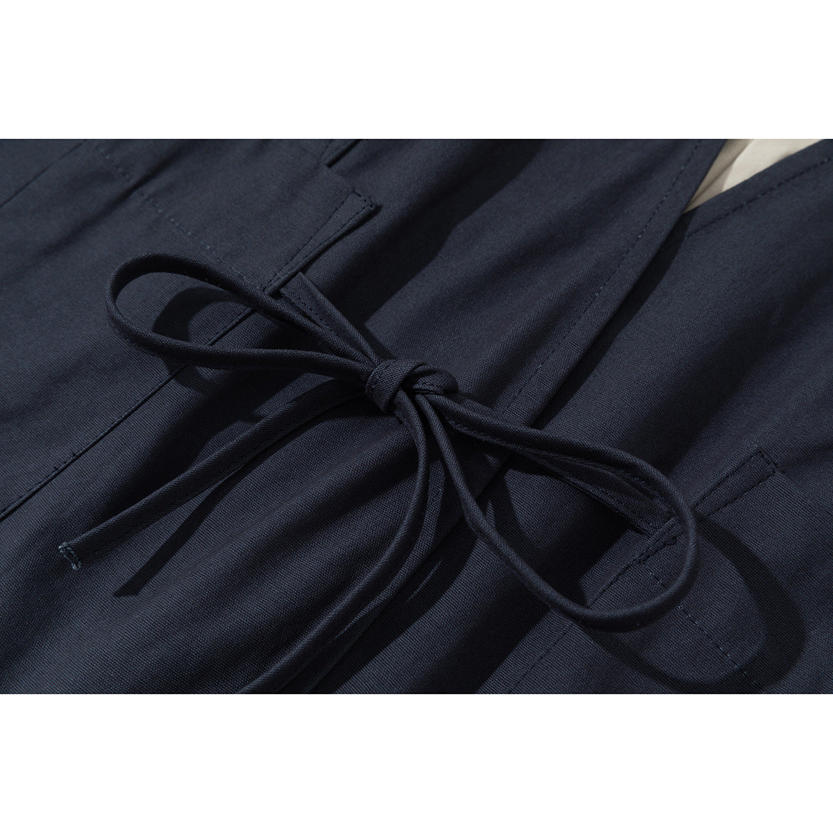 Close-up of a dark navy garment's tied waist cord and stitched loops.