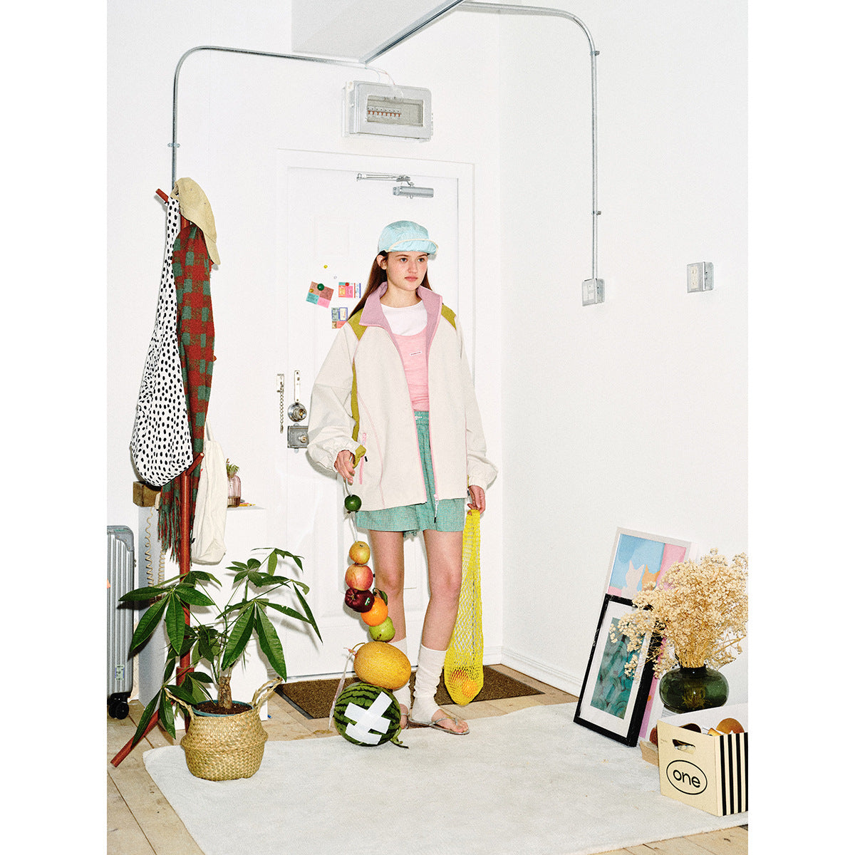 Model wears an ivory zip jacket with pink trim and olive accents over a pink top and turquoise shorts.