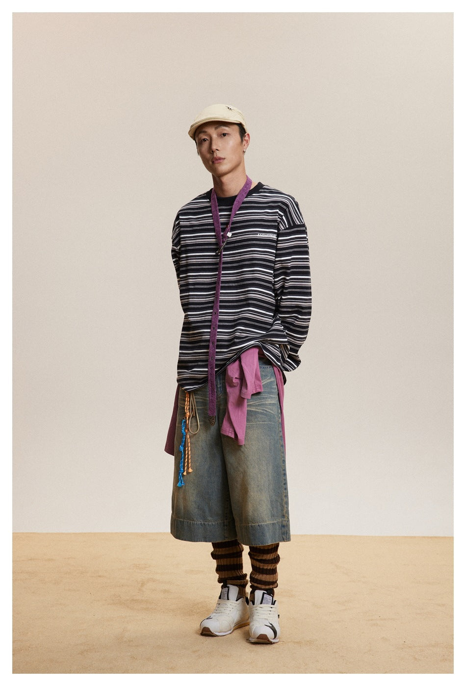 Model wearing the black striped long-sleeve top oversized with denim shorts, a cap and sneakers, front view