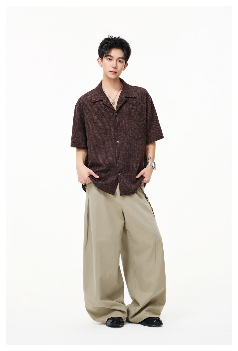 Full-length model wearing a brown short-sleeve button-up shirt with a notched collar and chest pocket.