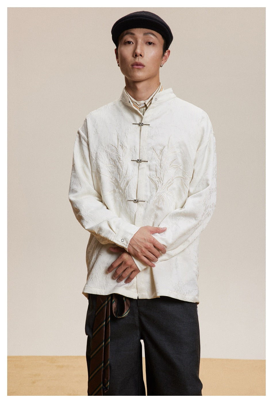 Front view of a model in an ivory embroidered jacket with a stand collar and metal frog closures.