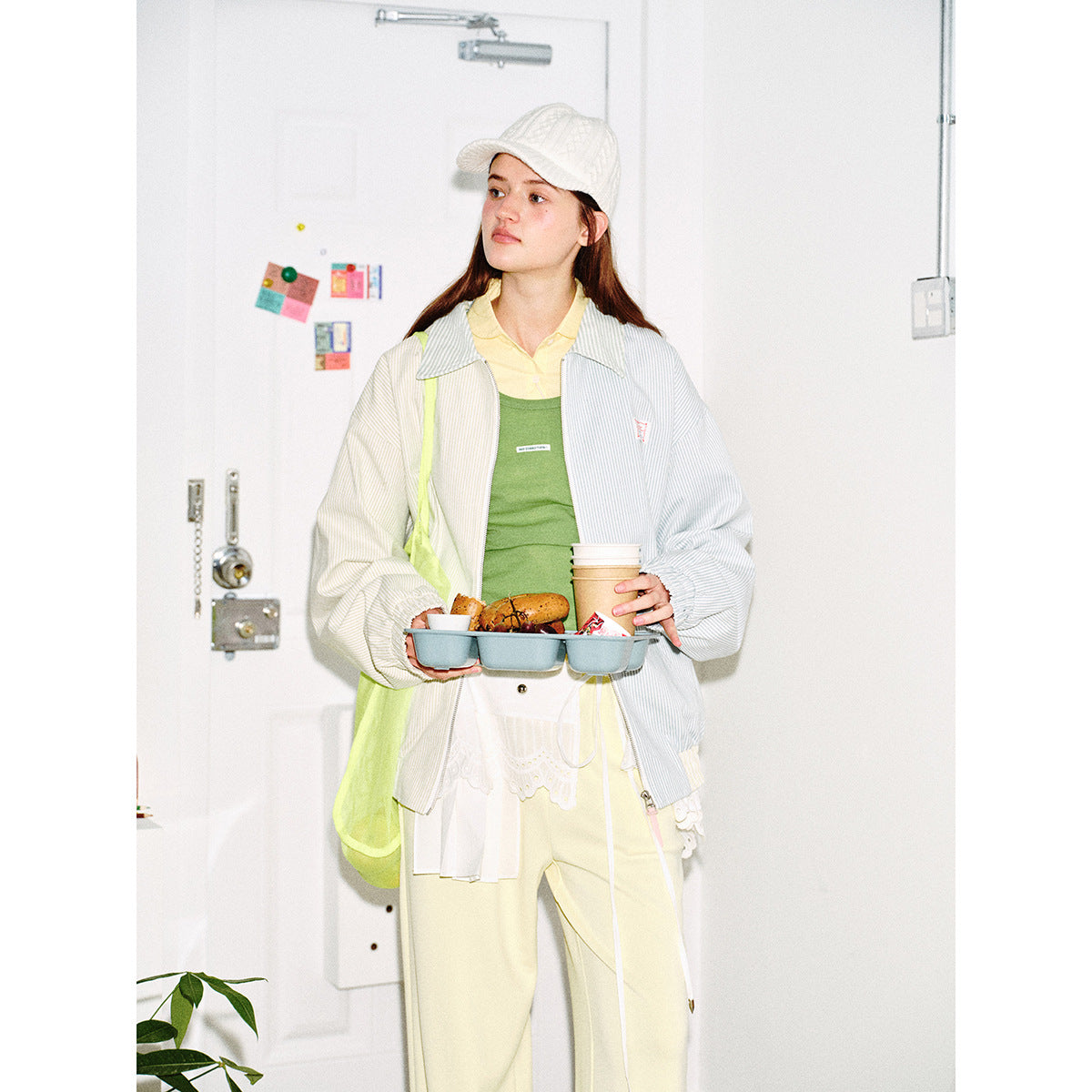 Closer view of a model in a pale blue and cream pinstriped zip jacket over a green top and yellow collared shirt.