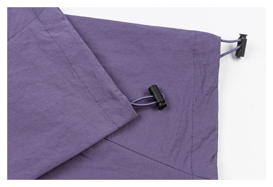 Close-up of purple pants showing a hem with cord loops and black adjustment toggles.
