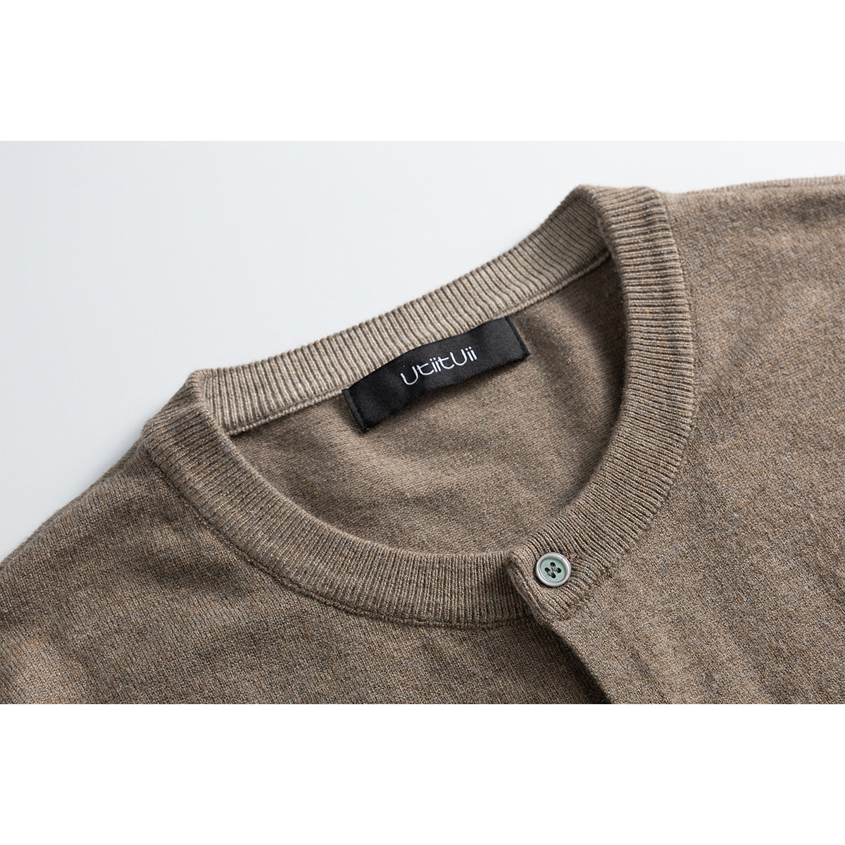 Close-up of a taupe-brown cardigan's ribbed crew neck, button, and inner neck label.