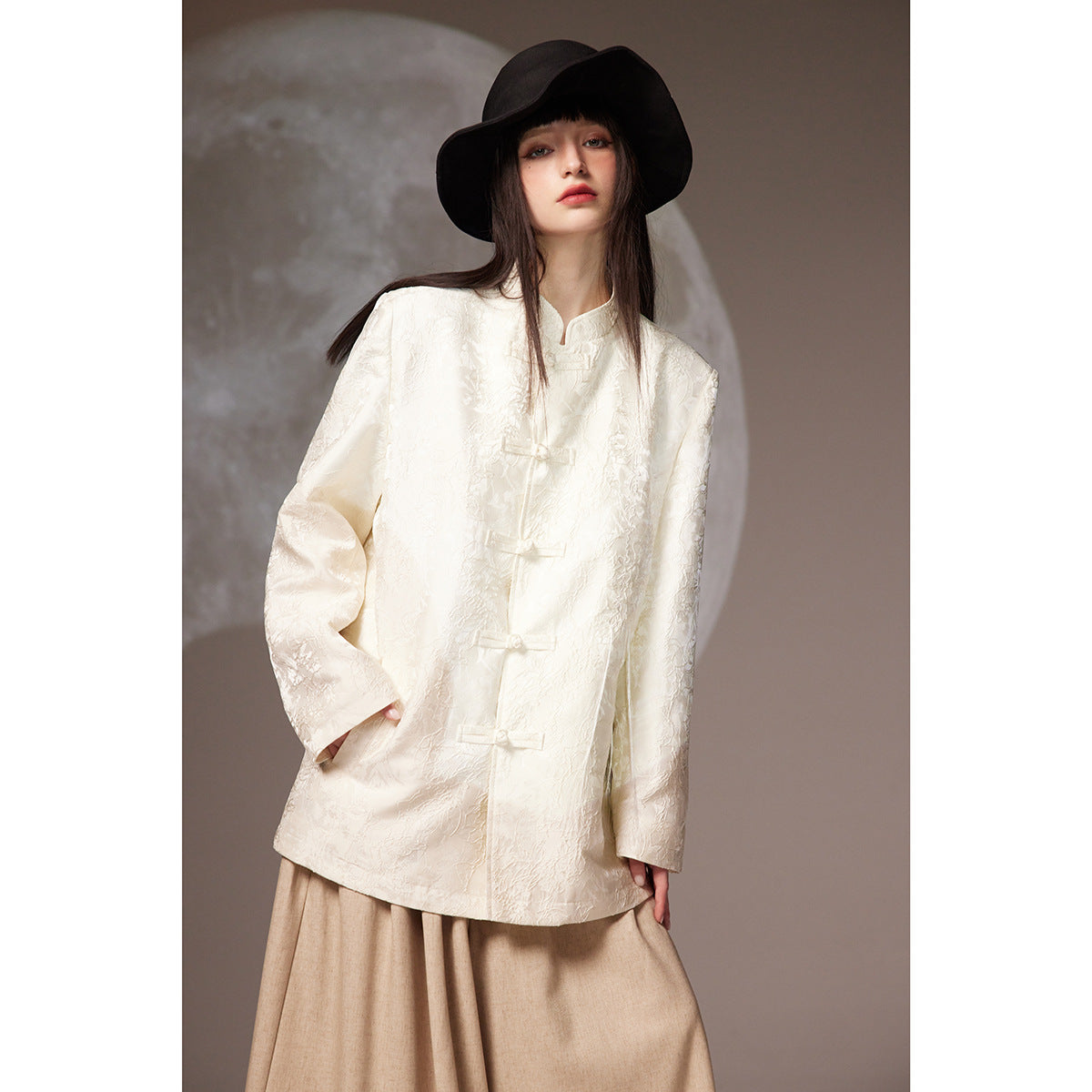 Model wearing an ivory floral jacquard frog-button jacket with a beige skirt and black wide-brim hat.