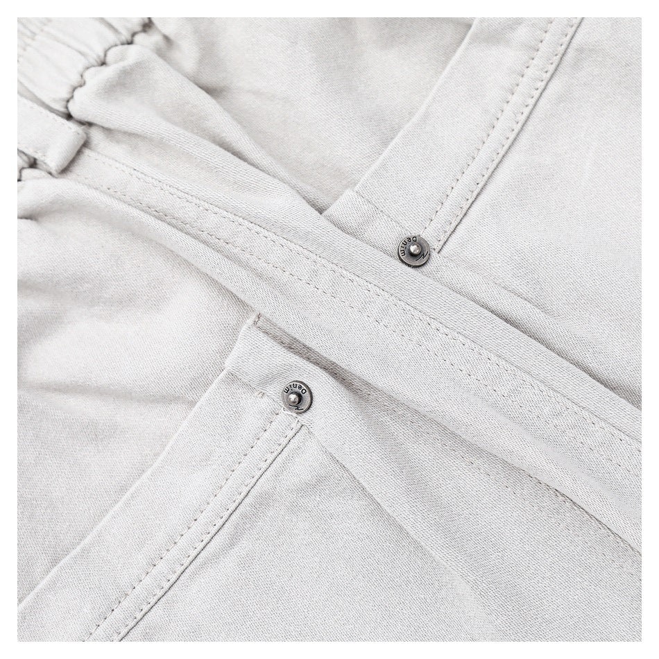 Close-up of light gray pants with an elastic waistband, stitched pocket edges and metal snap buttons.