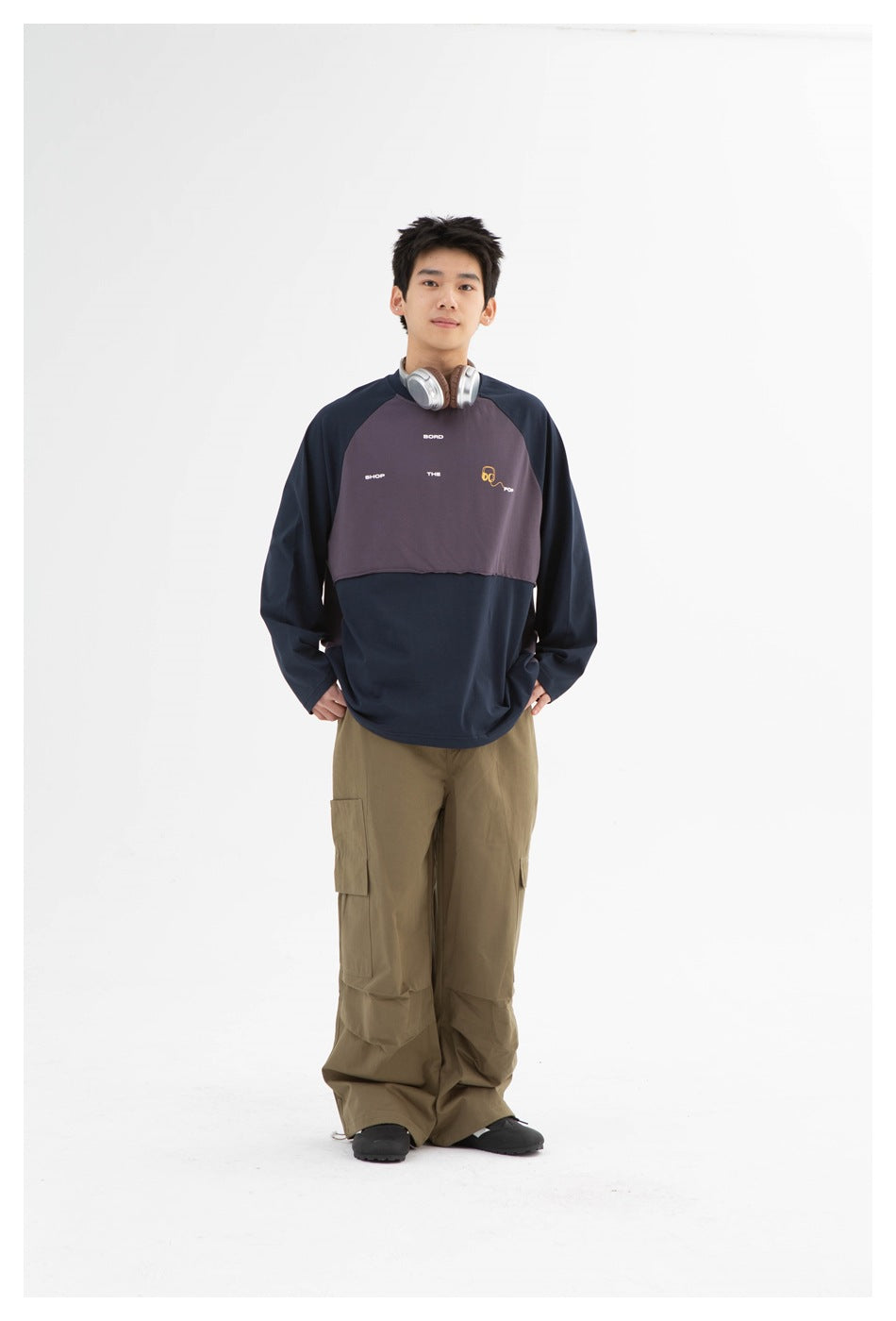 Model standing in navy and purple-gray color-block long-sleeve top with olive cargo pants and headphones around neck