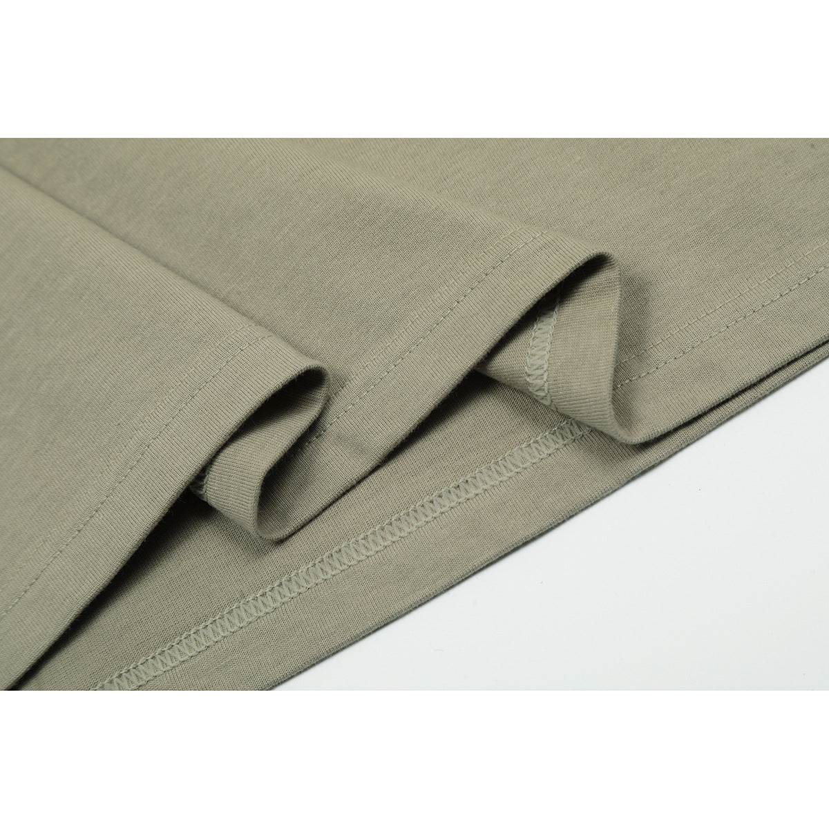 Close-up of the muted olive-gray T-shirt hem, showing folded fabric and overlock stitching.