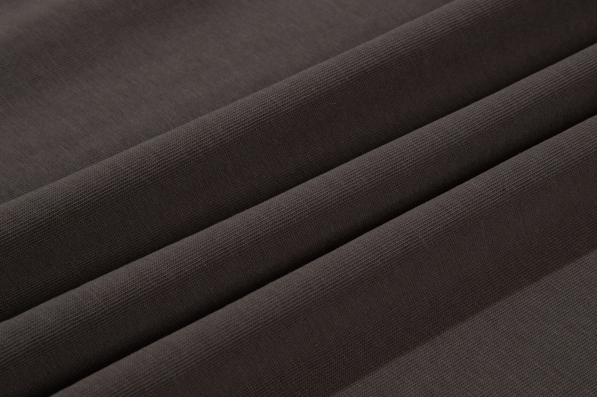 Macro view of dark brown fabric folded into diagonal ridges, showing its fine knit texture.