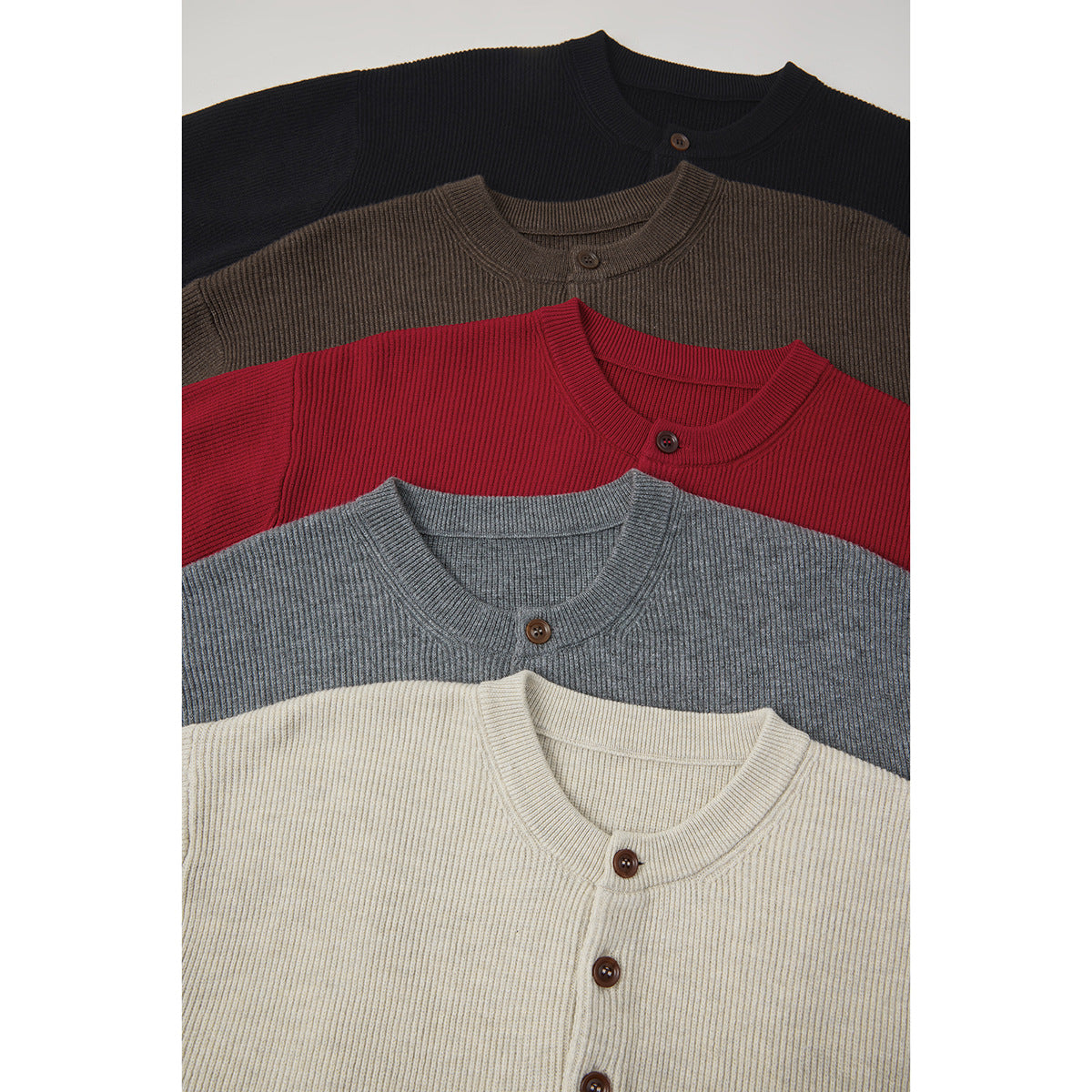 Overlapping ribbed button-neck sweaters in black, brown, red, gray, and cream, shown from the front.